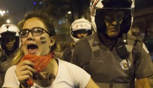 Imagem de capa do Livro Escola Pública. Tempos difíceis, mas não impossíveis mostra uma estudante se manifestando e um policial ao seu lado